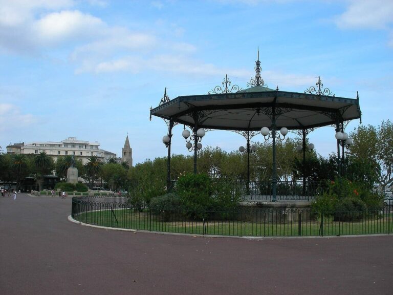 Le kiosque à musique de la place Saint-Nicolas, entouré d’un jardin clôturé, avec le clocher d’une église au loin