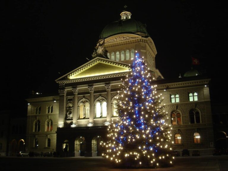 Le Palais fédéral de Berne éclairé la nuit, avec un sapin de Noël orné de lumières blanches et bleues