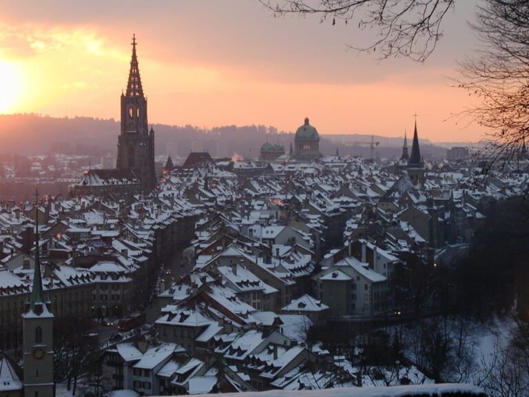 Les toits enneigés de la vieille ville de Berne au coucher du soleil, dominés par la flèche de la collégiale