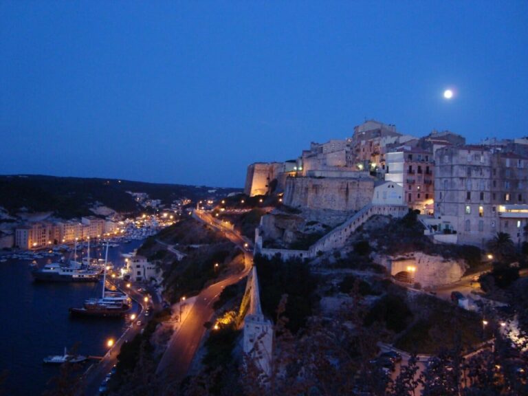 La Haute-Ville de Bonifacio éclairée au-dessus du port, à la nuit tombante, la lune dans le ciel
