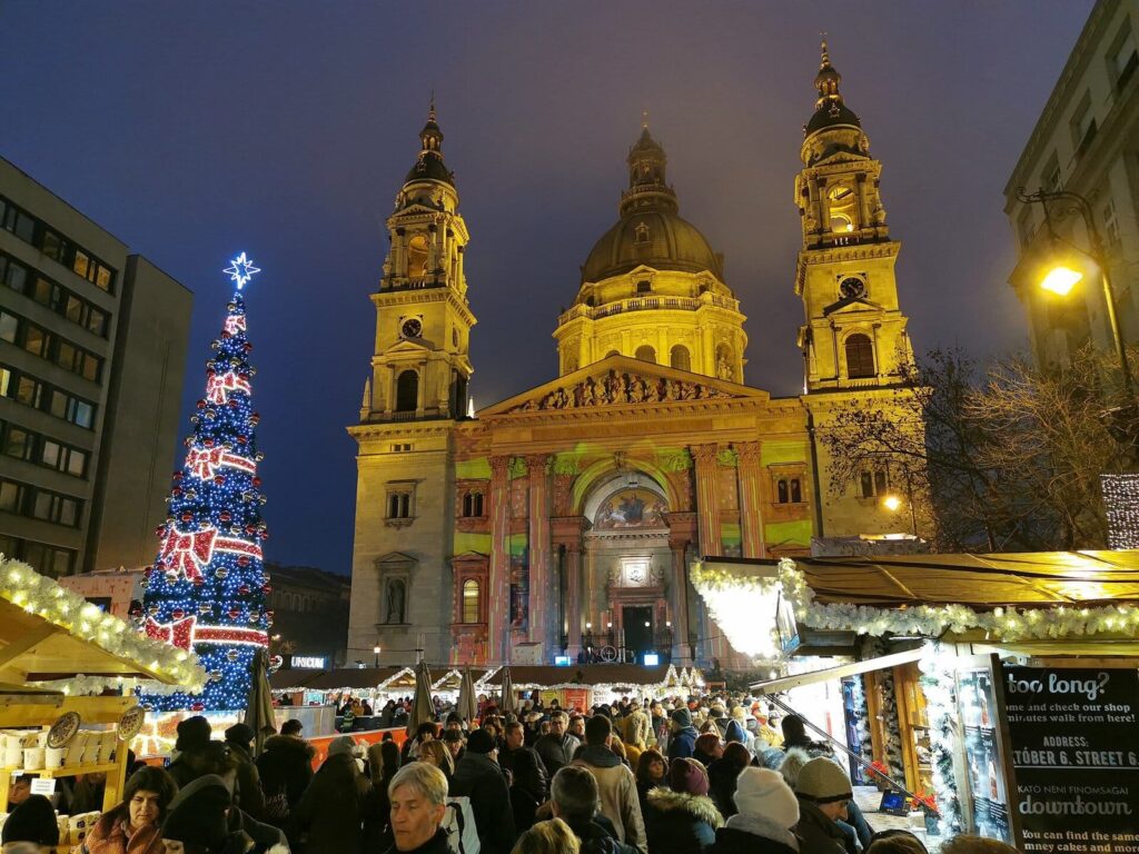 La basilique Saint-Étienne éclairée de nuit au-dessus des chalets du marché de l’Avent, avec le grand sapin décoré au pied de la façade