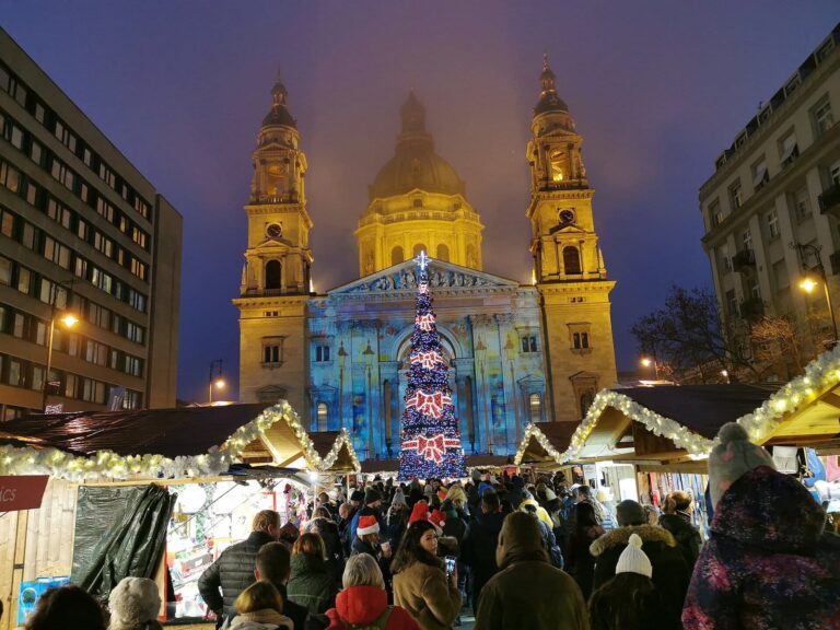 La façade de la basilique Saint-Étienne animée par des projections de lumière, au-dessus des toits des chalets du marché de l’Avent