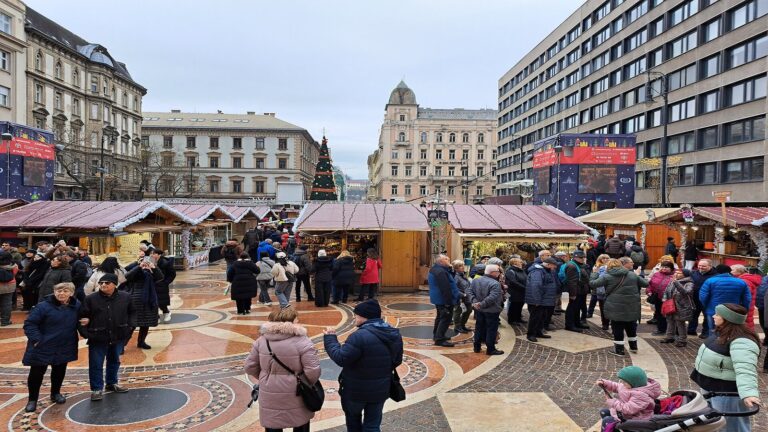 La place Saint-Étienne de Budapest en journée, avec la rangée de chalets du marché de Noël, le sapin au loin et le dallage en mosaïque au premier plan