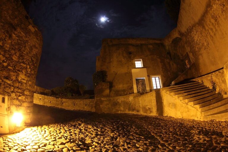 Une rue pavée de la citadelle de Calvi éclairée la nuit, sous la lune