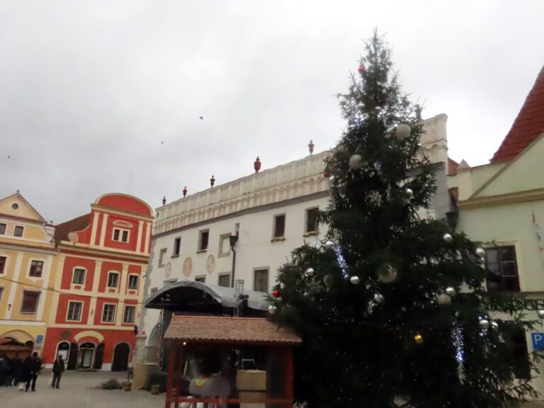 Le sapin de Noël et un chalet du marché sur la place Svornosti de Český Krumlov, devant l’hôtel de ville et ses maisons colorées, le 24 décembre