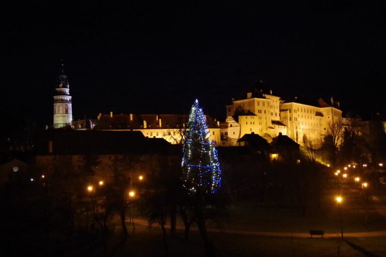 Le château de Český Krumlov et sa tour illuminés de nuit, avec un sapin de Noël éclairé en contrebas
