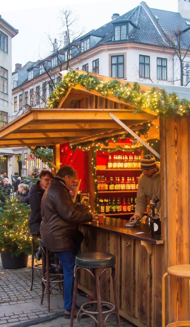 Un chalet-bar en bois décoré de branches de sapin au marché de Noël de Copenhague, devant des immeubles danois