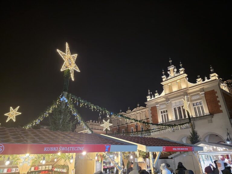 Une étoile lumineuse au sommet d’un sapin et des étals devant les Halles aux draps, sur le Rynek Główny, de nuit