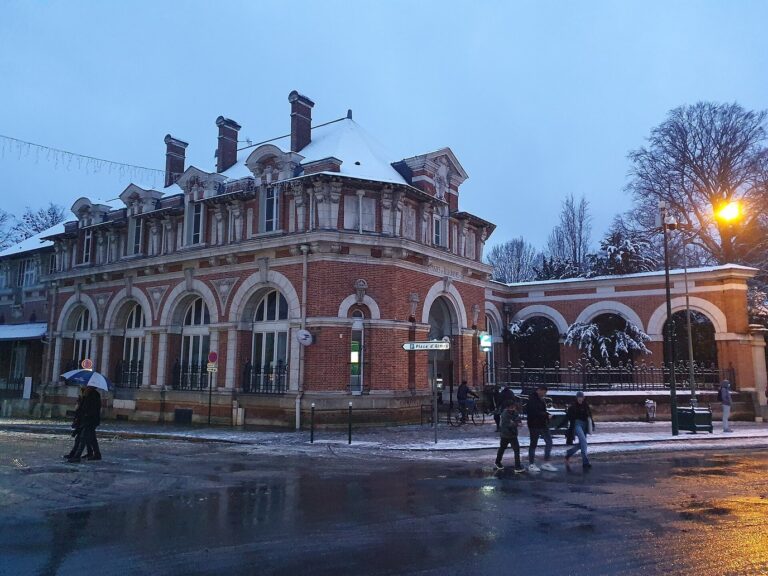 L’hôtel des Postes en briques rouges sous la neige, au crépuscule, avec une guirlande lumineuse tendue au-dessus de la rue
