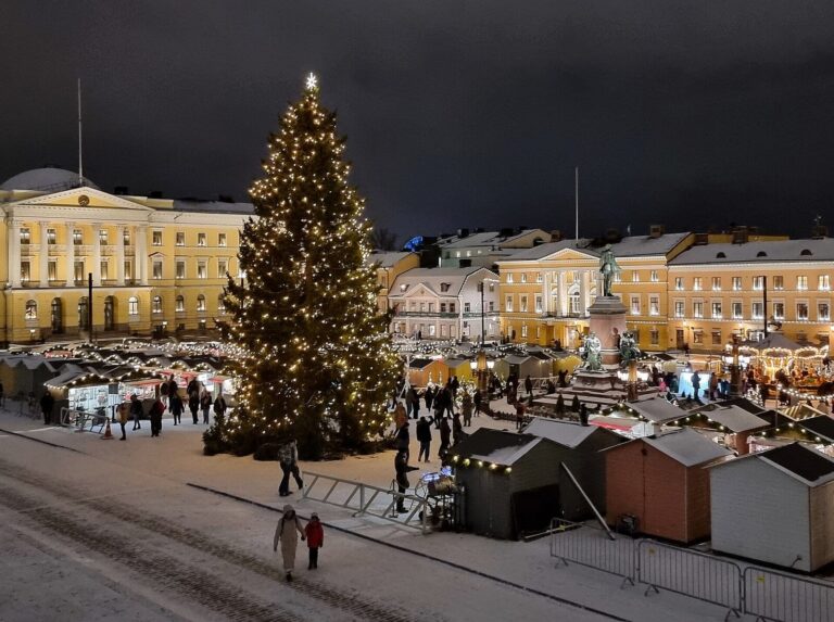 La place du Sénat d’Helsinki de nuit pendant le marché de Noël, le sapin illuminé, les chalets et la statue d’Alexandre II dans la lumière des façades