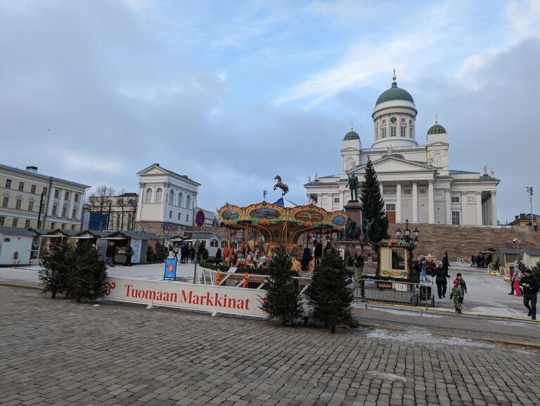 Le manège du marché de Noël Tuomaan Markkinat et la cathédrale d’Helsinki en hiver, avec le bandeau du marché et de petits sapins au premier plan