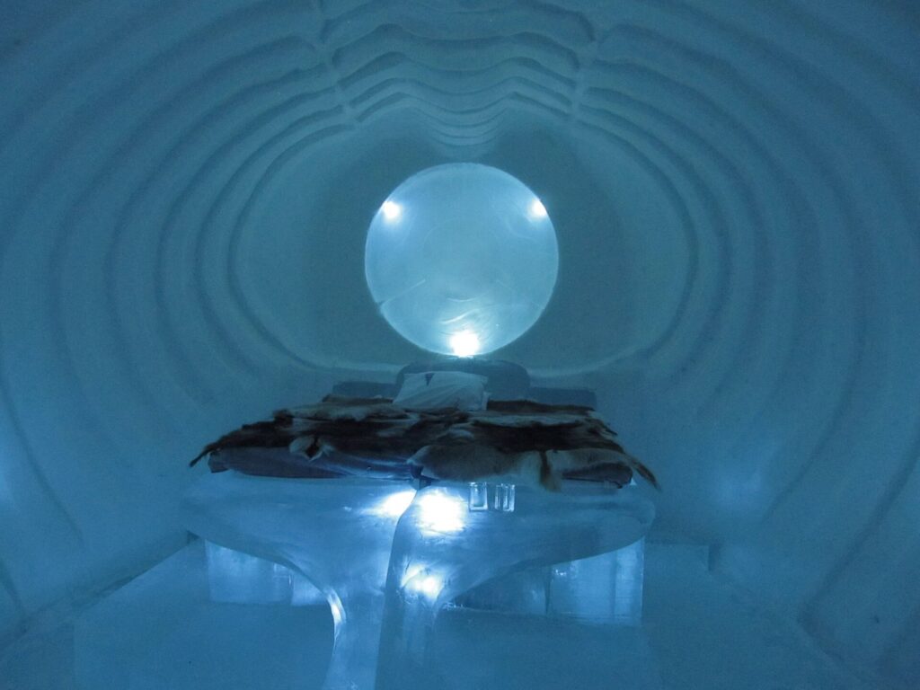 Une chambre de glace de l’Icehotel avec un lit sous une sphère lumineuse et des parois sculptées en anneaux