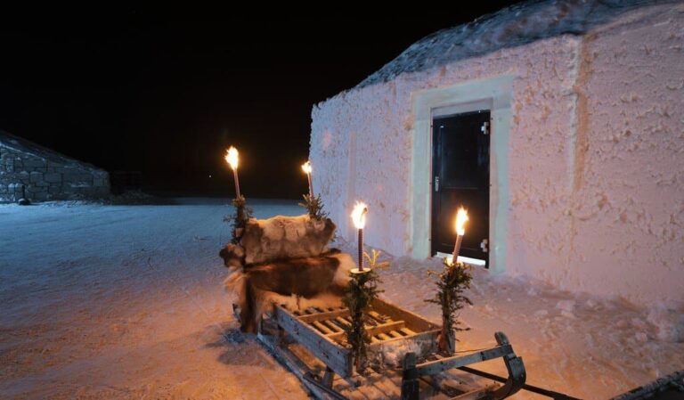 Un traîneau garni de fourrure et de flambeaux allumés devant une porte de l’Icehotel, le soir de Noël