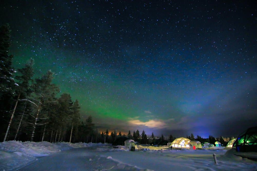 Des igloos de verre éclairés dans le village de Kakslauttanen, sous un ciel étoilé et une aurore verte