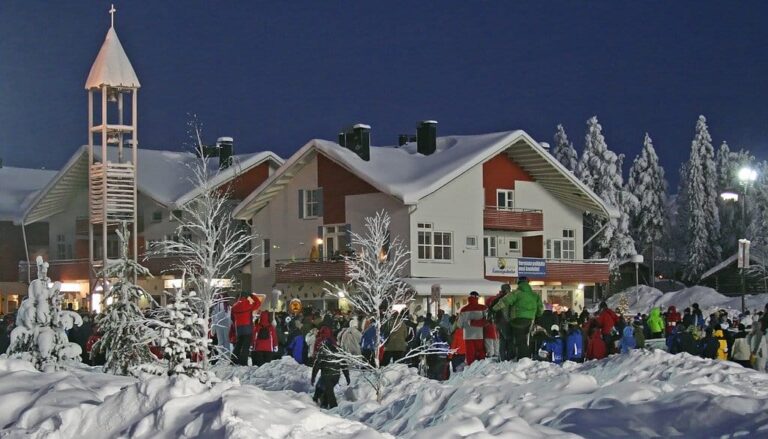 La foule rassemblée de dos devant les chalets enneigés et le clocher de bois de Levi, le soir de la déclaration de la paix de Noël