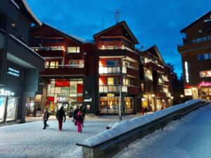Les immeubles de bois rouge du centre de Levi éclairés au crépuscule, au-dessus d’une rue piétonne enneigée
