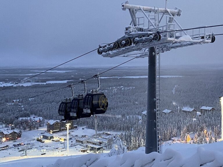 Une télécabine sous un pylône givré, au-dessus de la forêt enneigée et des chalets de Levi