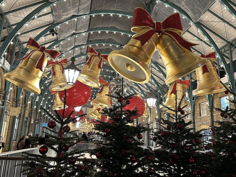 De grandes cloches dorées nouées de rubans rouges suspendues sous la verrière de Covent Garden Market, avec un sapin au premier plan