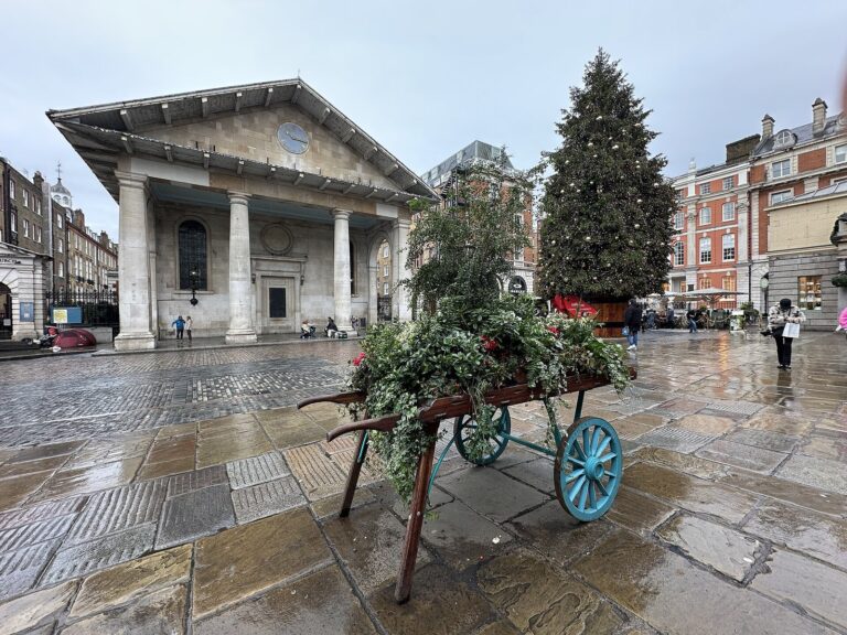 Un sapin de Noël décoré devant l’église Saint-Paul et un chariot fleuri de branchages, sur la piazza de Covent Garden un jour de pluie