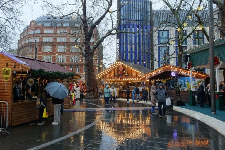 L’allée des chalets du marché de Noël de Leicester Square sous la pluie, avec le reflet des guirlandes sur le sol mouillé