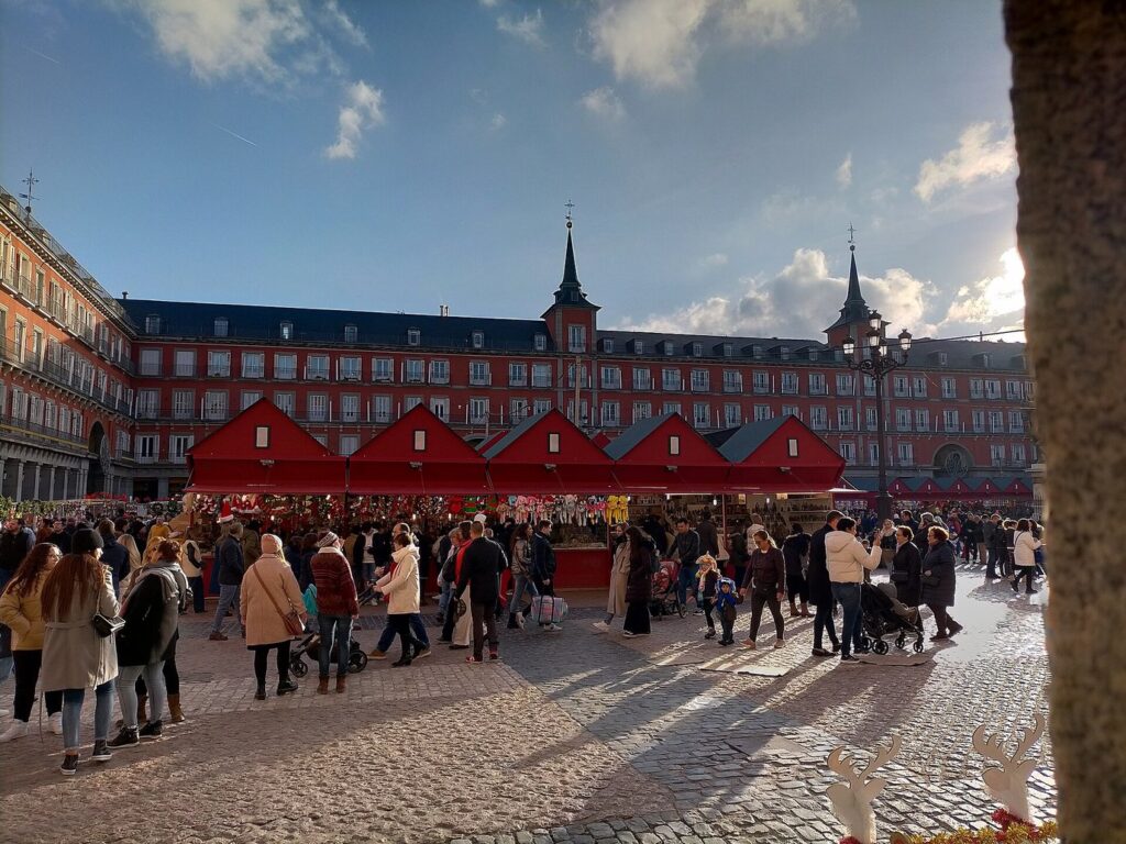 Les chalets rouges du marché de Noël de la Plaza Mayor de Madrid, devant les façades à arcades et les deux tours de la place, sous un ciel d’hiver