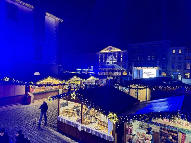 Les chalets illuminés du marché de Noël d’Olomouc sous les façades éclairées en bleu, de nuit