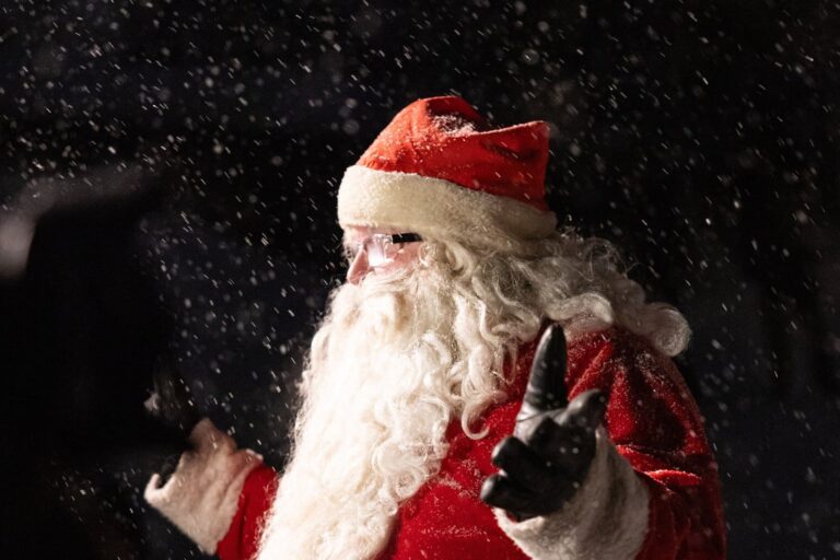 Le Père Noël lève la main sous la neige qui tombe, de nuit, à Saariselkä, en décembre 2024