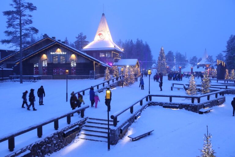 La place du Santa Claus Village à l’heure bleue, avec la flèche éclairée du bureau du Père Noël et des sapins illuminés, à Rovaniemi