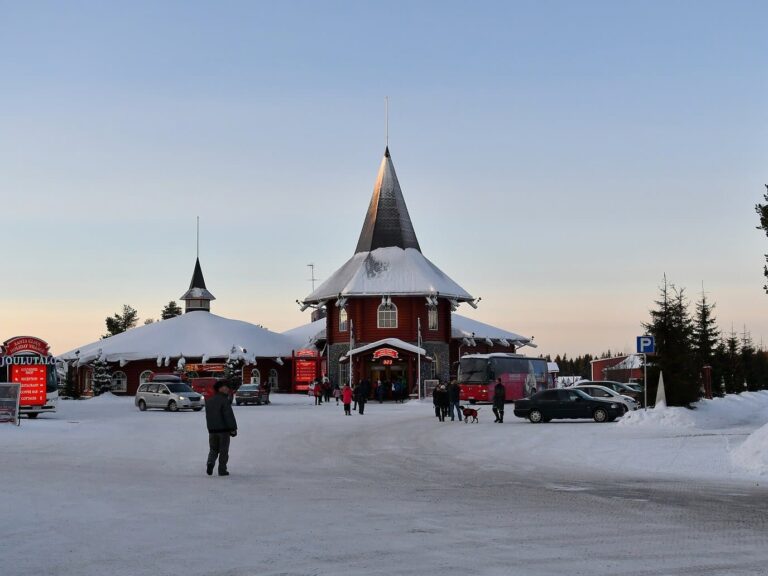 La maison de Noël du village et sa flèche rouge et noire au crépuscule, au bout d’une place enneigée