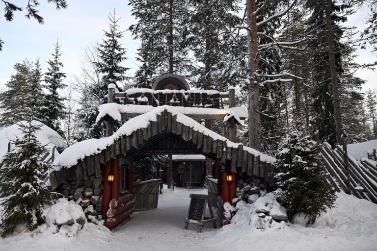 Un portail de bois au toit couvert de neige, entre les sapins du Santa Claus Village