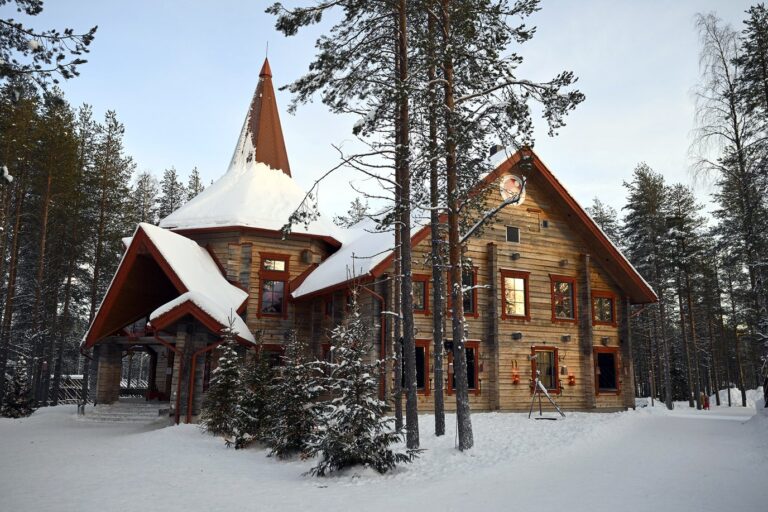 Un grand chalet de bois au toit pointu, entouré de pins et de neige, dans le Santa Claus Village
