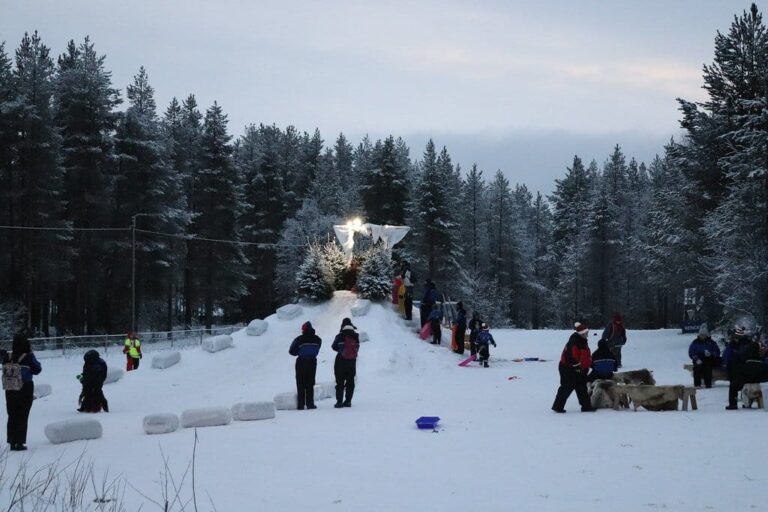 La piste de luge enneigée de SantaPark entre les sapins, avec des visiteurs au loin