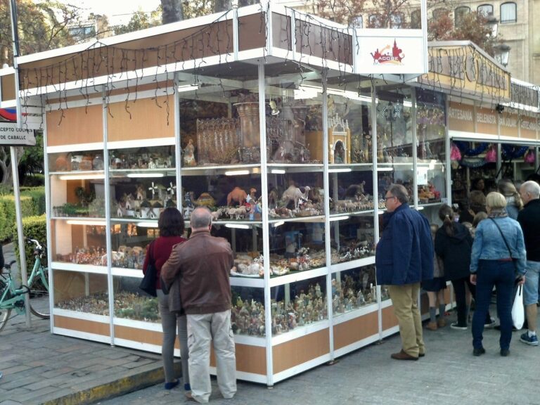 Des visiteurs devant un stand vitré de la Feria del Belén rempli de figurines et de décors de crèche