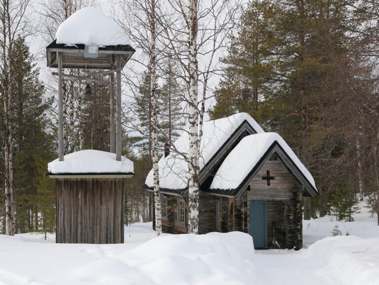 La petite chapelle de rondins de Lainio et son clocher de bois, sous la neige, dans un bois de bouleaux