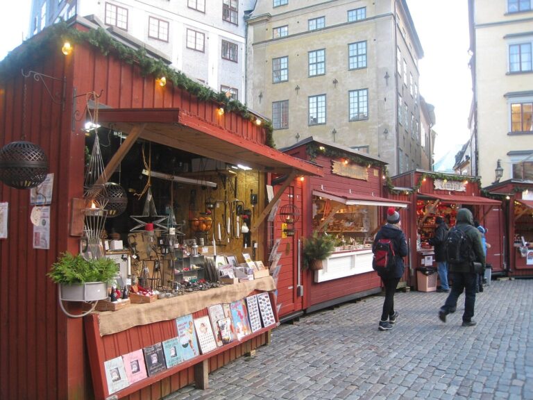 Étal de vannerie et d’ustensiles dans un chalet rouge du marché de Noël de Stortorget, sous des branches de sapin