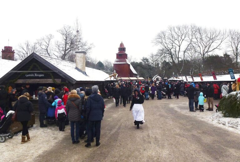 L’allée enneigée du musée de plein air de Skansen pendant le marché de Noël, avec les chalets et les visiteurs au loin