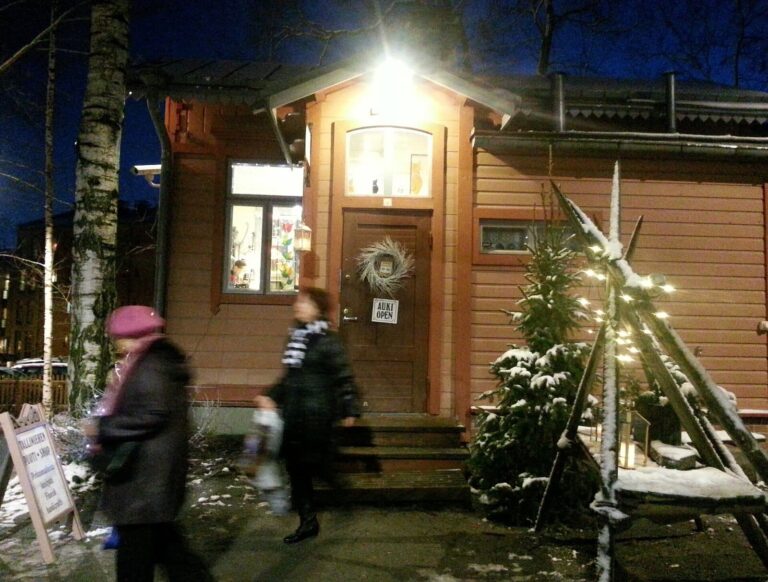 Une maisonnette en bois rose de la cour Tallipiha de Tampere, illuminée de nuit avec des guirlandes de Noël et un peu de neige