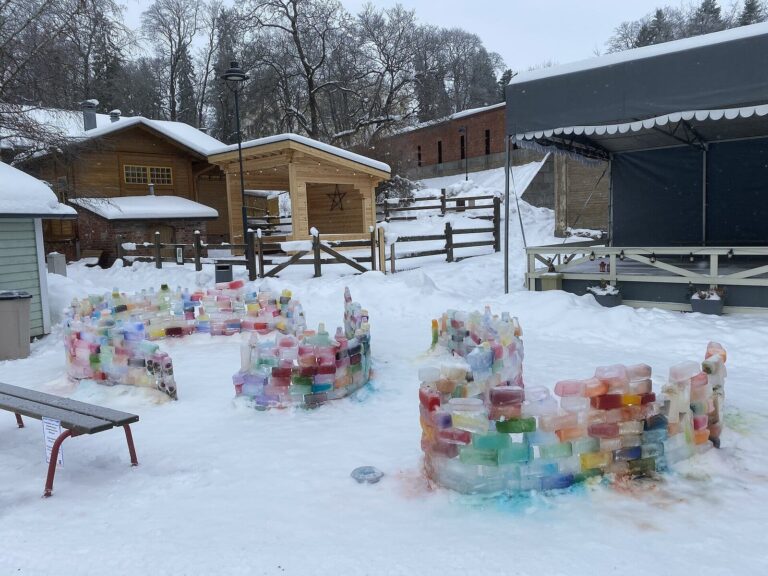 Des murets de briques de glace colorées dans la cour Tallipiha de Tampere en hiver, devant les petites maisons en bois enneigées