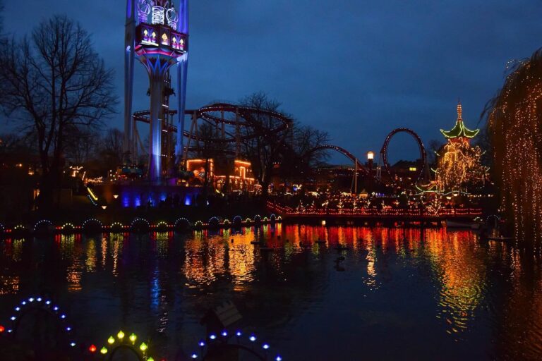 Le lac de Tivoli au crépuscule, avec la tour des balançoires et les montagnes russes illuminées de l’autre côté de l’eau