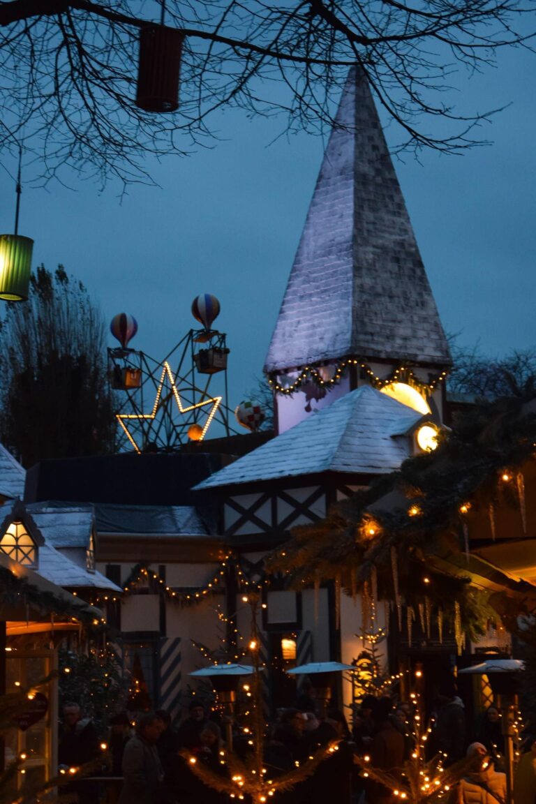 Un clocher blanc et des maisons à colombages décorés de lumières et de sapins dans le marché de Noël de Tivoli, de nuit