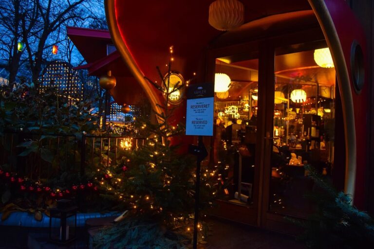 Un restaurant aux grandes baies rouges de Tivoli, entouré de sapins et de guirlandes lumineuses, au crépuscule