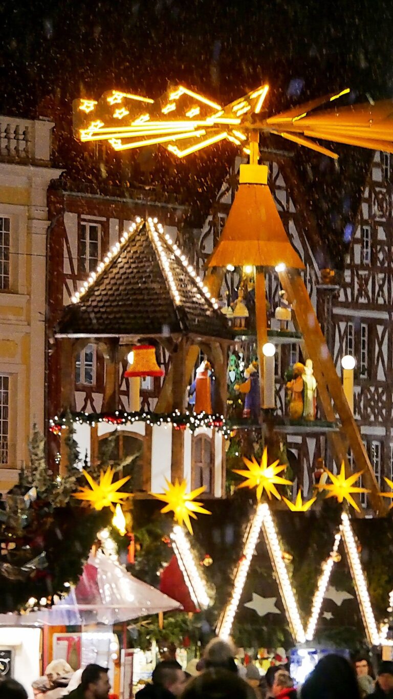 Pyramide de Noël en bois éclairée au-dessus d’un stand de l’Erzgebirge, la nuit, devant une façade à colombages