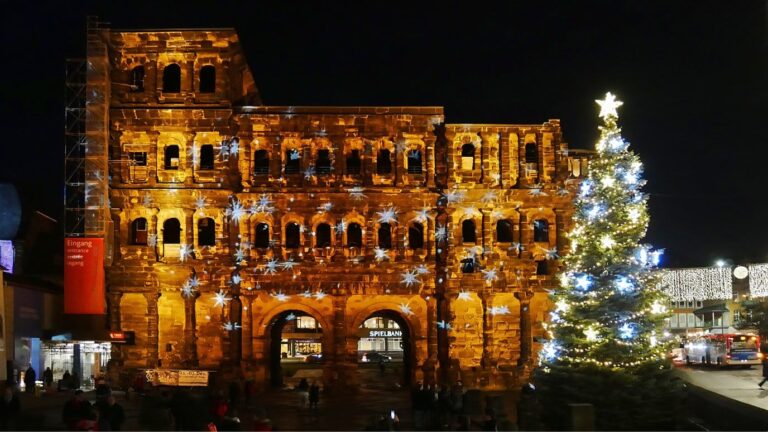 La Porta Nigra romaine éclairée la nuit, à côté d’un sapin de Noël illuminé d’une étoile