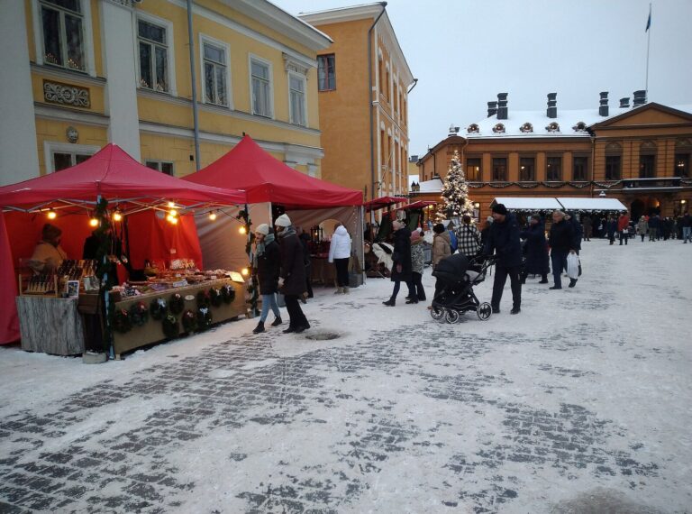 Les chalets à toits rouges du marché de Noël de la Vieille Grand-Place de Turku sur la neige, avec les maisons jaunes et la maison Brinkkala au fond