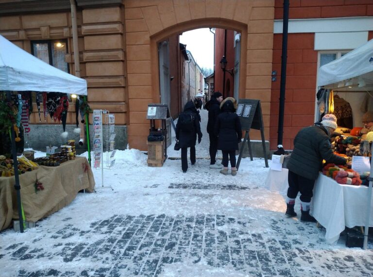 Des étals de produits d’artisanat devant un passage voûté d’un bâtiment ocre de la Vieille Grand-Place de Turku, sur la neige