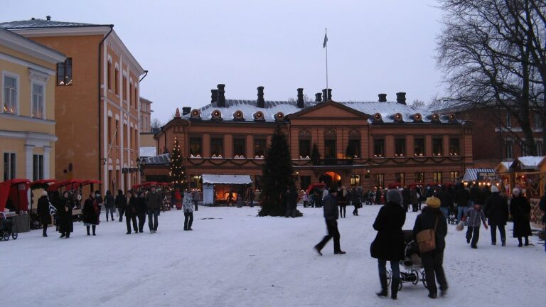 La Vieille Grand-Place de Turku enneigée au marché de Noël, avec un sapin devant la maison Brinkkala et des étals rouges sur le côté