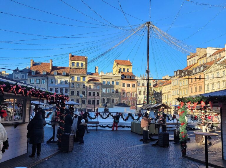 Les chalets du marché de Noël de la place du Marché de la vieille ville de Varsovie, ornés de guirlandes, vus depuis la patinoire, sous un ciel bleu