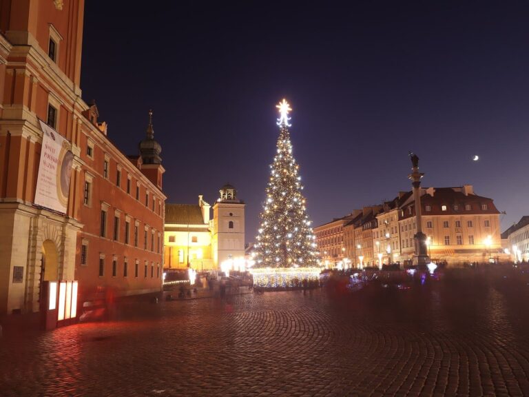 La place du Château de Varsovie de nuit, avec le château royal à gauche, un sapin illuminé au centre et la colonne de Sigismond au fond