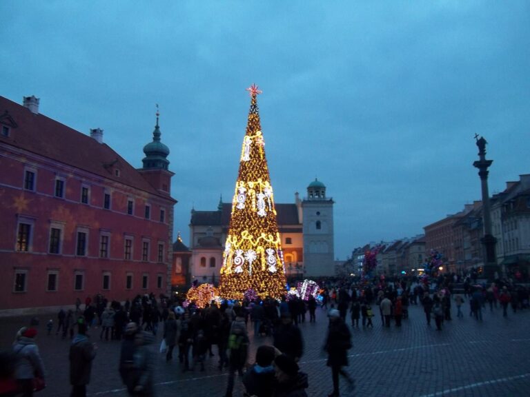 Le sapin de Noël illuminé de la place du Château de Varsovie au crépuscule, avec les passants, le château royal et la colonne de Sigismond