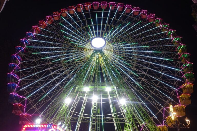 La grande roue de Noël de Vigo illuminée de nuit, vue d’en bas, ses rayons verts et ses nacelles éclairées de rose et de jaune